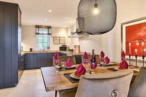 A modern dining area with a wooden table set for four, a hanging light fixture, and a view of the kitchen in the background. - Holiday apartment with 2 bedrooms (Munkmarsch)