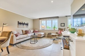 A modern living room with a sofa, armchairs, a coffee table, and a kitchen area with cabinets and a window. - Holiday apartment with 2 bedrooms (Munkmarsch)