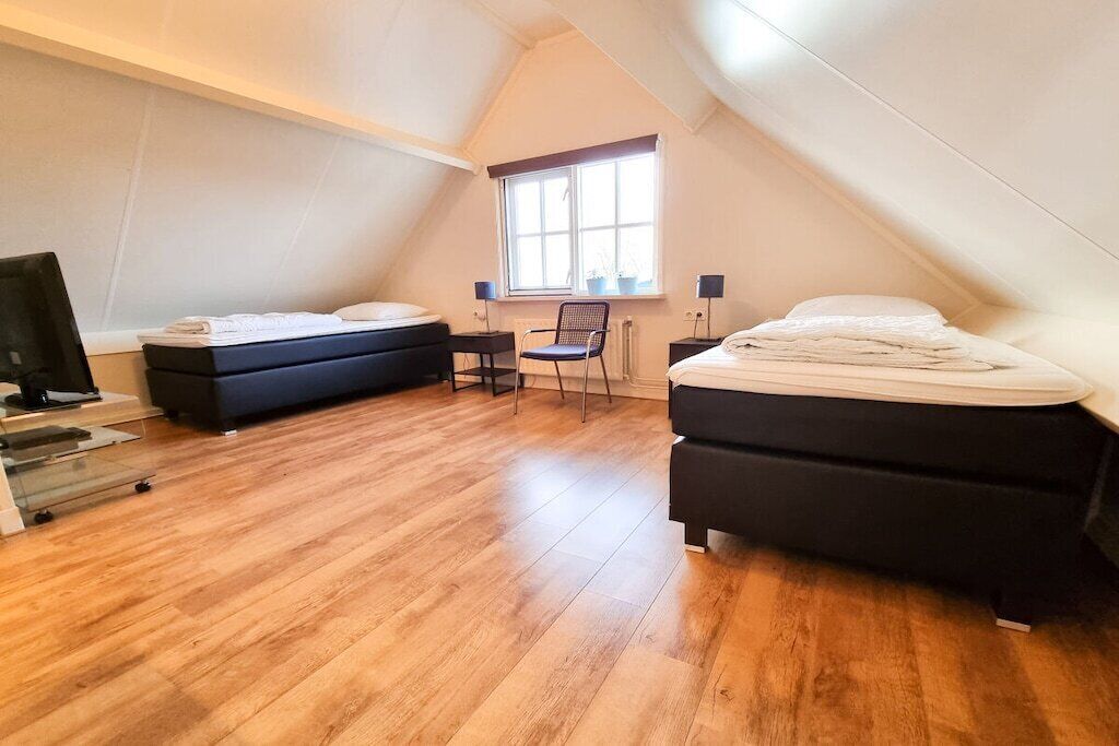 A bedroom with two beds, a desk, a chair, a TV, and a window.