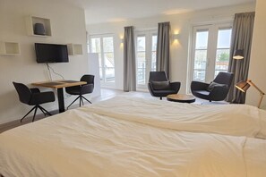 A hotel room with a large bed, a desk with a chair, a TV mounted on the wall, and a view of the outside through large windows. - DO06 Holiday home Domburg (Domburg)