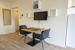A modern living room with a flat-screen TV mounted on the wall, a wooden coffee table, two black chairs, and a white refrigerator. - DO06 Holiday home Domburg (Domburg)