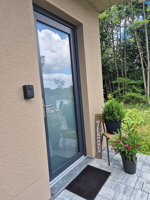 Eine Tür mit Fenster, ein Willkommensschild, ein Blumentopf und eine Bank.