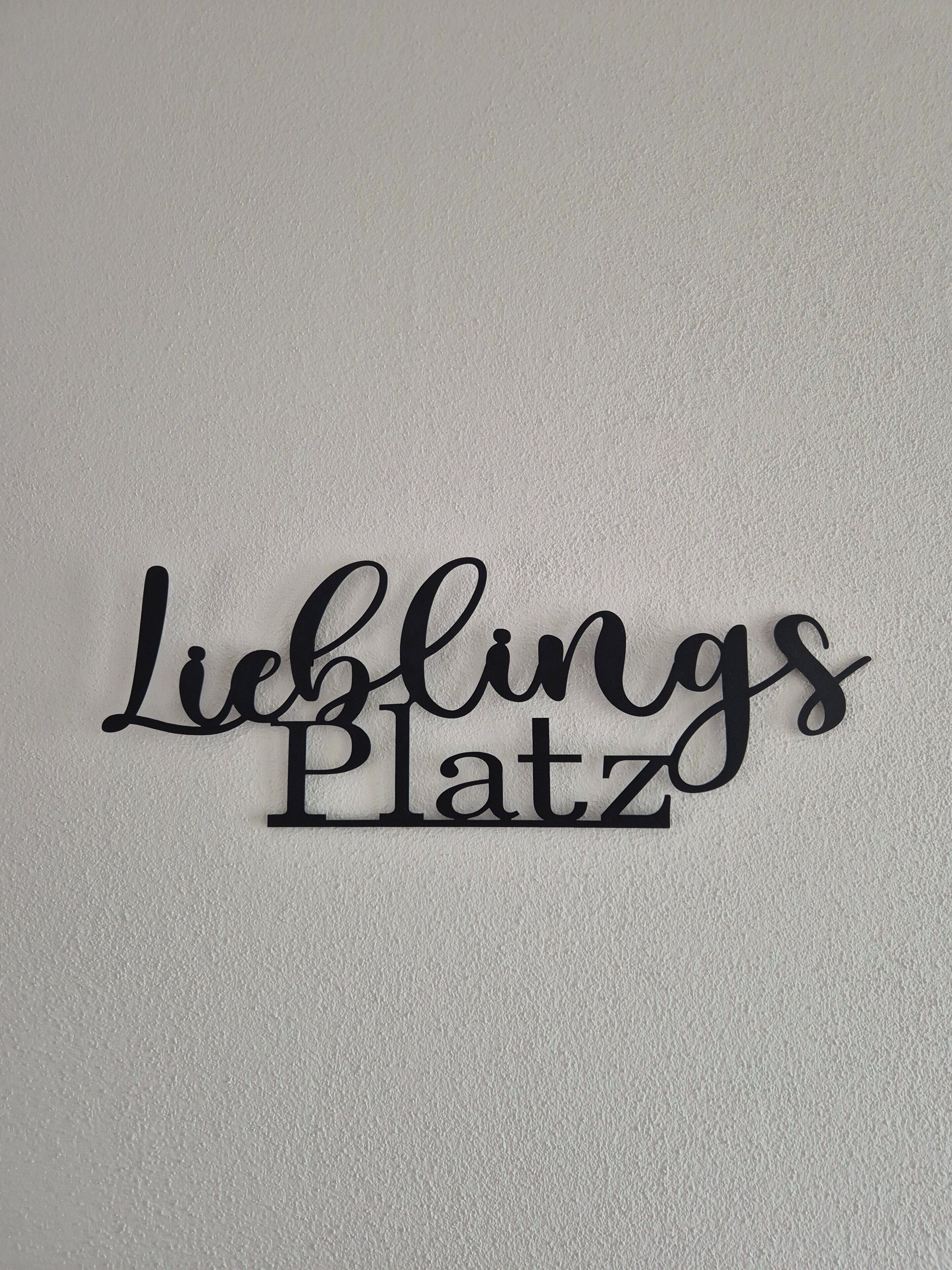 Een bord aan de muur met de woorden 'Lieblings Platz' in een sierlijk lettertype.