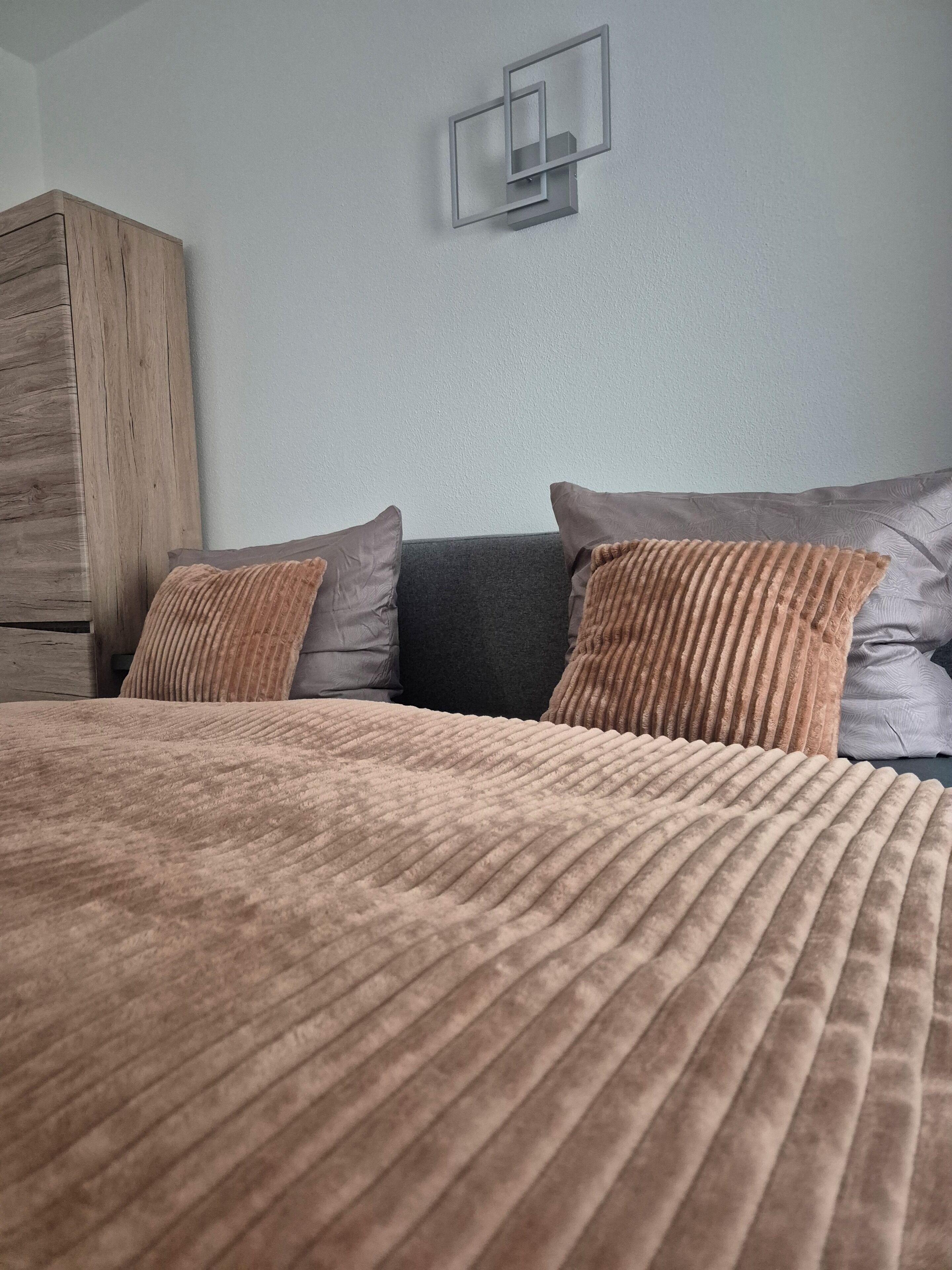 Ein Schlafzimmer mit einem Bett, Kissen, einem Holzschrank und einer Wandleuchte.