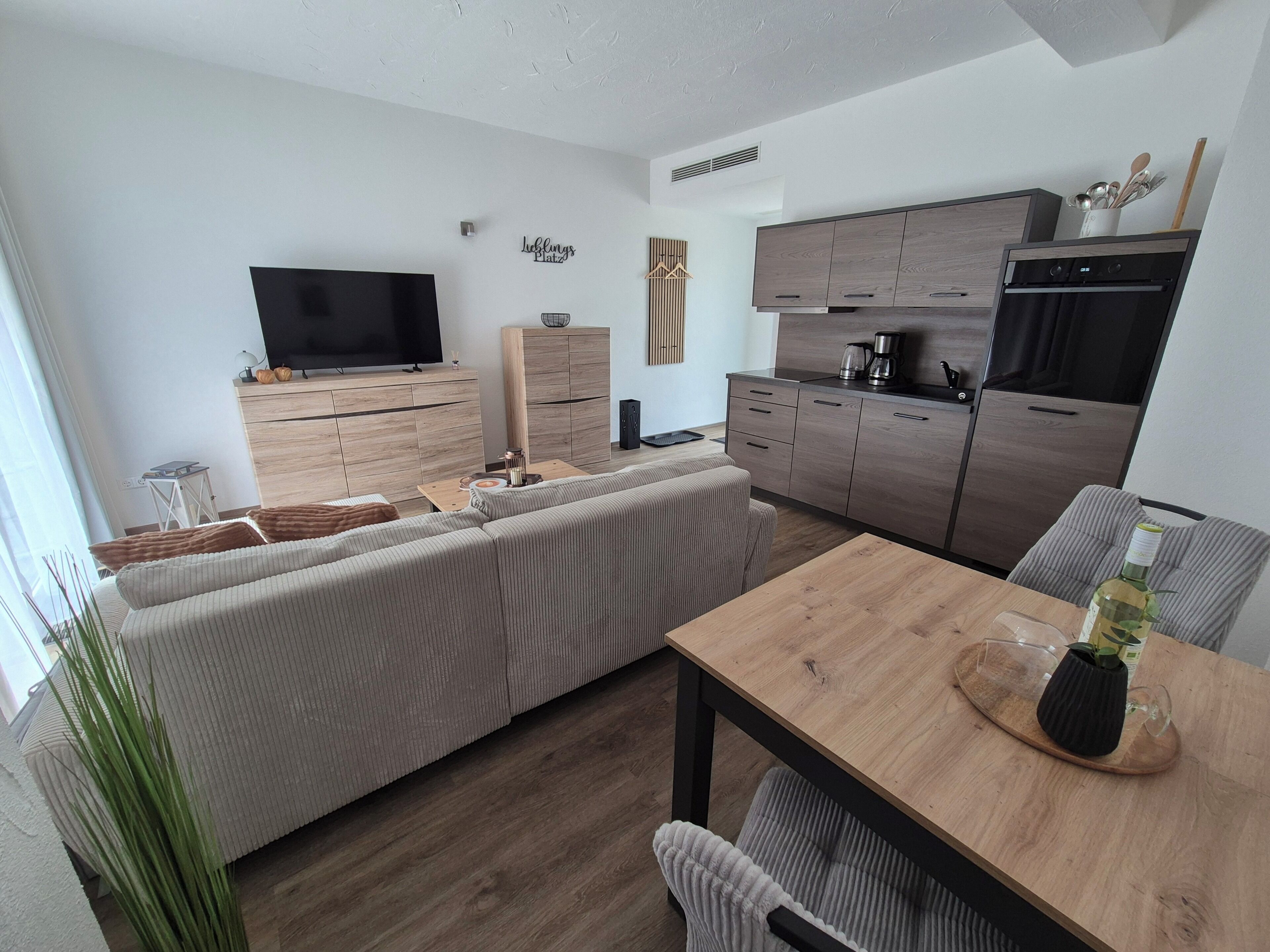 Ein stilvoller Wohnraum mit Sofa, Esstisch, Küchenzeile und Flachbildfernseher.