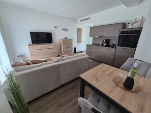 A modern living space with a sofa, dining table, kitchen area, and a flat-screen TV.