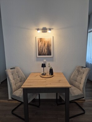 Ein Essbereich mit Holztisch, zwei Stühlen, einer Wandleuchte und einem gerahmten Bild.