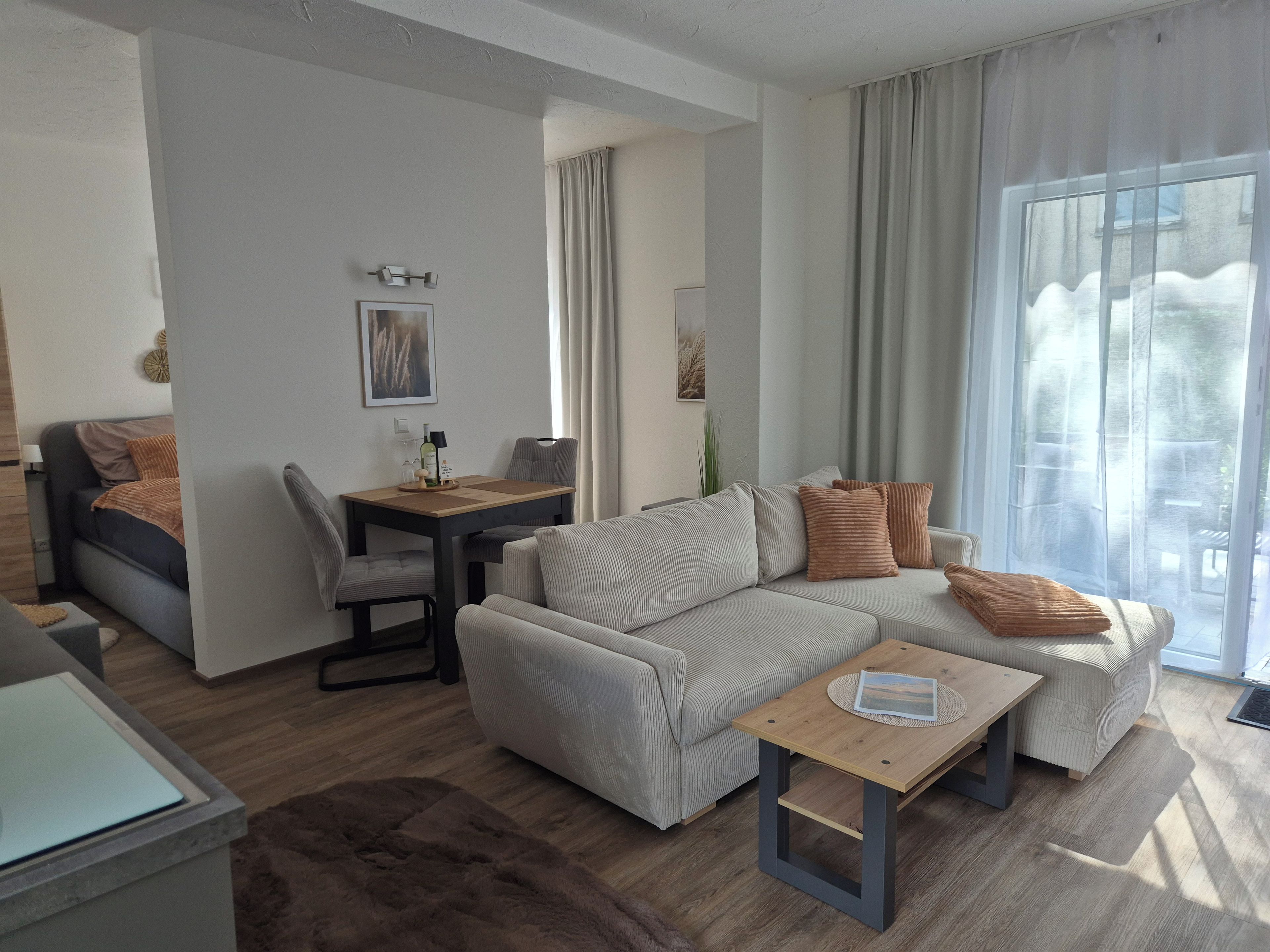 Ein modernes Wohnzimmer mit einer Couch, einem Couchtisch, einem Esstisch mit Stühlen und einem großen Fenster mit Vorhängen.