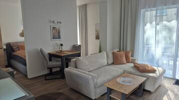 En moderne stue med sofa, sofabord, spisebord med stole og et stort vindue med gardiner.