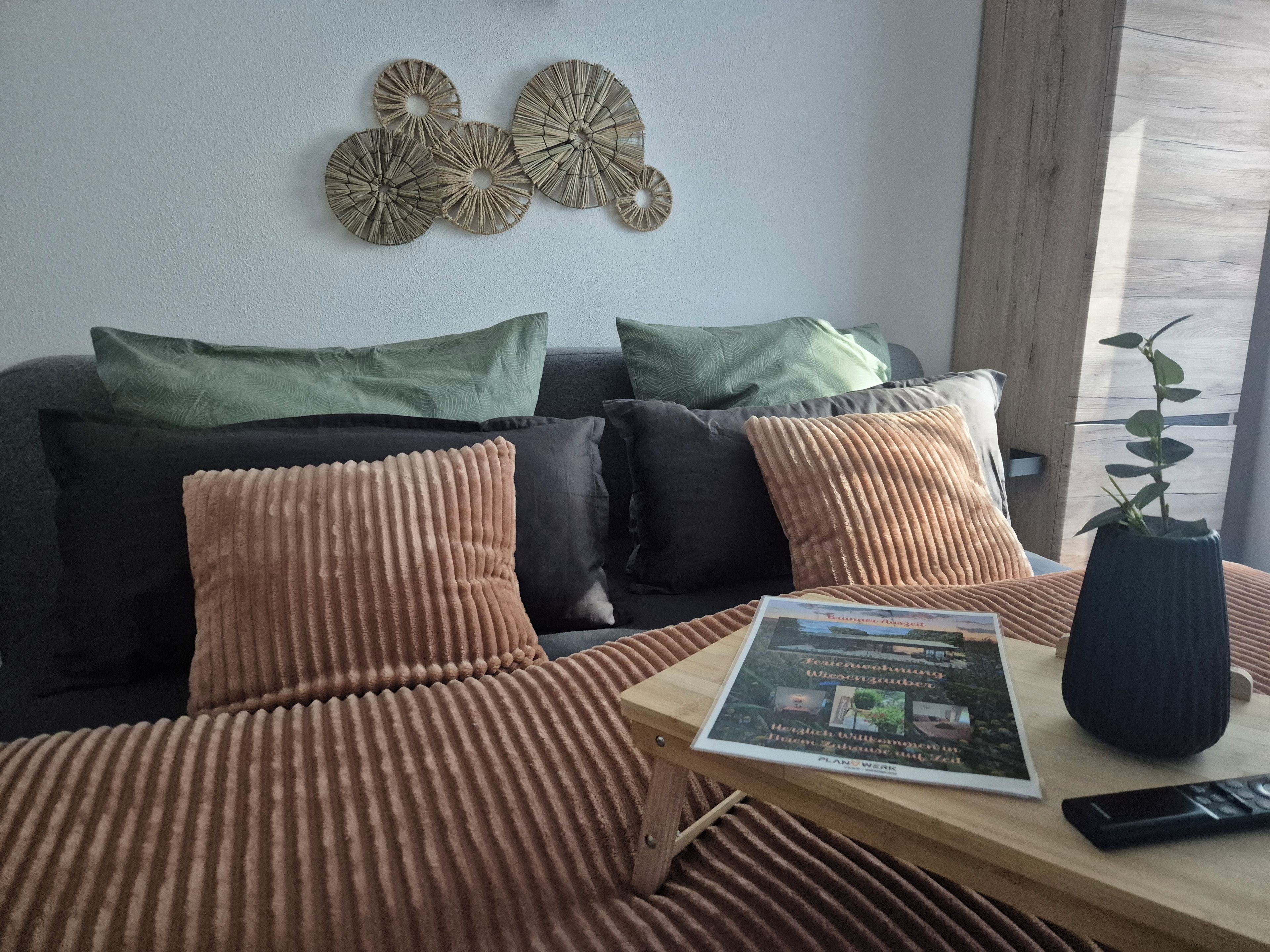 Ein stilvolles Wohnzimmer mit einer Couch, Kissen, einem Couchtisch, einer Fernbedienung und einem Buch.