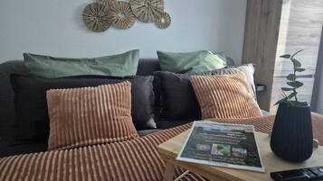 Ein stilvolles Wohnzimmer mit einer Couch, Kissen, einem Couchtisch, einer Fernbedienung und einem Buch.
