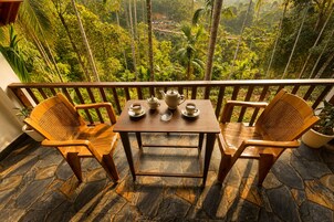 Een balkon met twee houten stoelen en een tafel, een bloempot en uitzicht op een weelderig groon landschap.