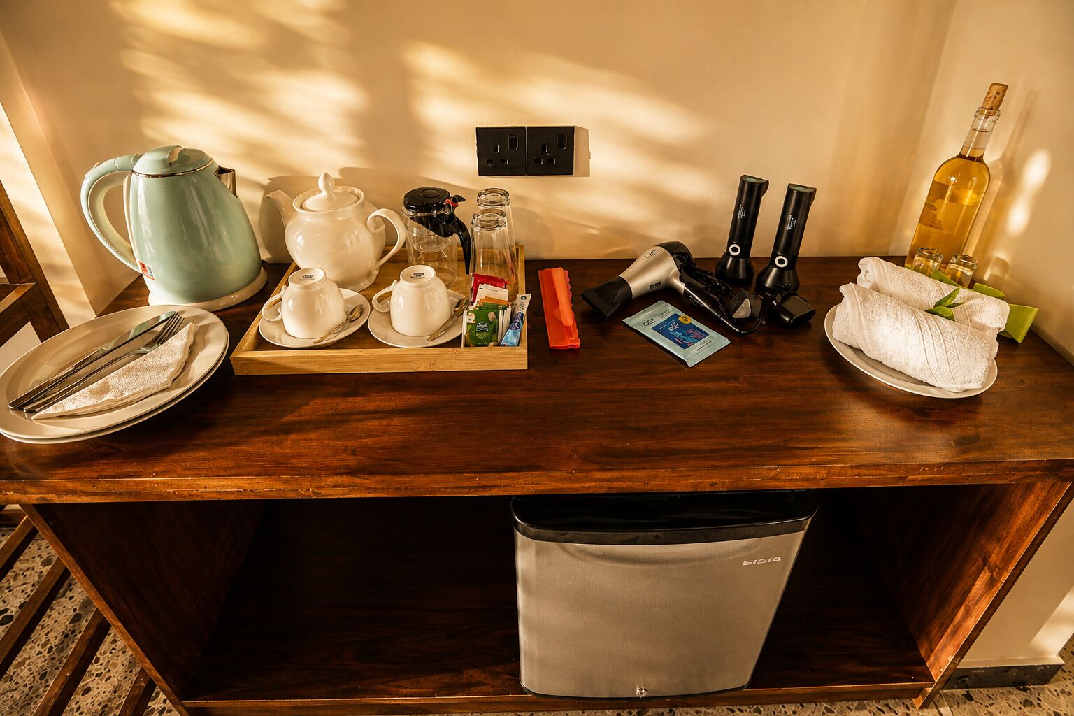 Balcão de madeira para refeições com máquina de café, chá e acompanhamentos.