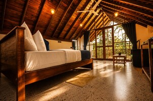 Una habitación amplia con una cama grande, techo de madera y vistas por un ventanal.
