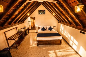 Un dormitorio con techo inclinado, vigas de madera, una cama con almohadas, una mesita de noche y un estante montado en la pared.