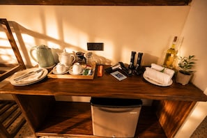 Escritorio de madera con un cubo de basura, una tetera, tazas de té, una botella y una planta.