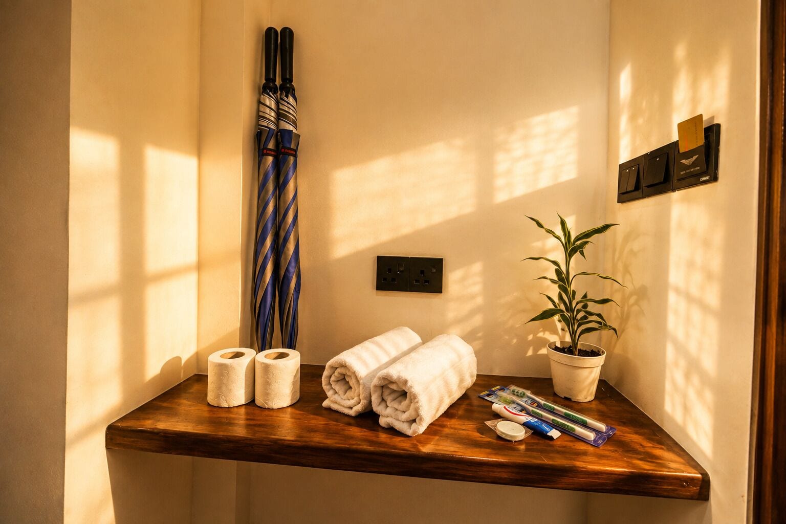 A bathroom with a wooden vanity, towels, a striped umbrella, a potted plant, and a towel dispenser.