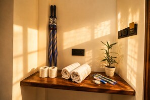 Un baño con tocador de madera, toallas, un paraguas a rayas, una planta en maceta y un dispensador de toallas.