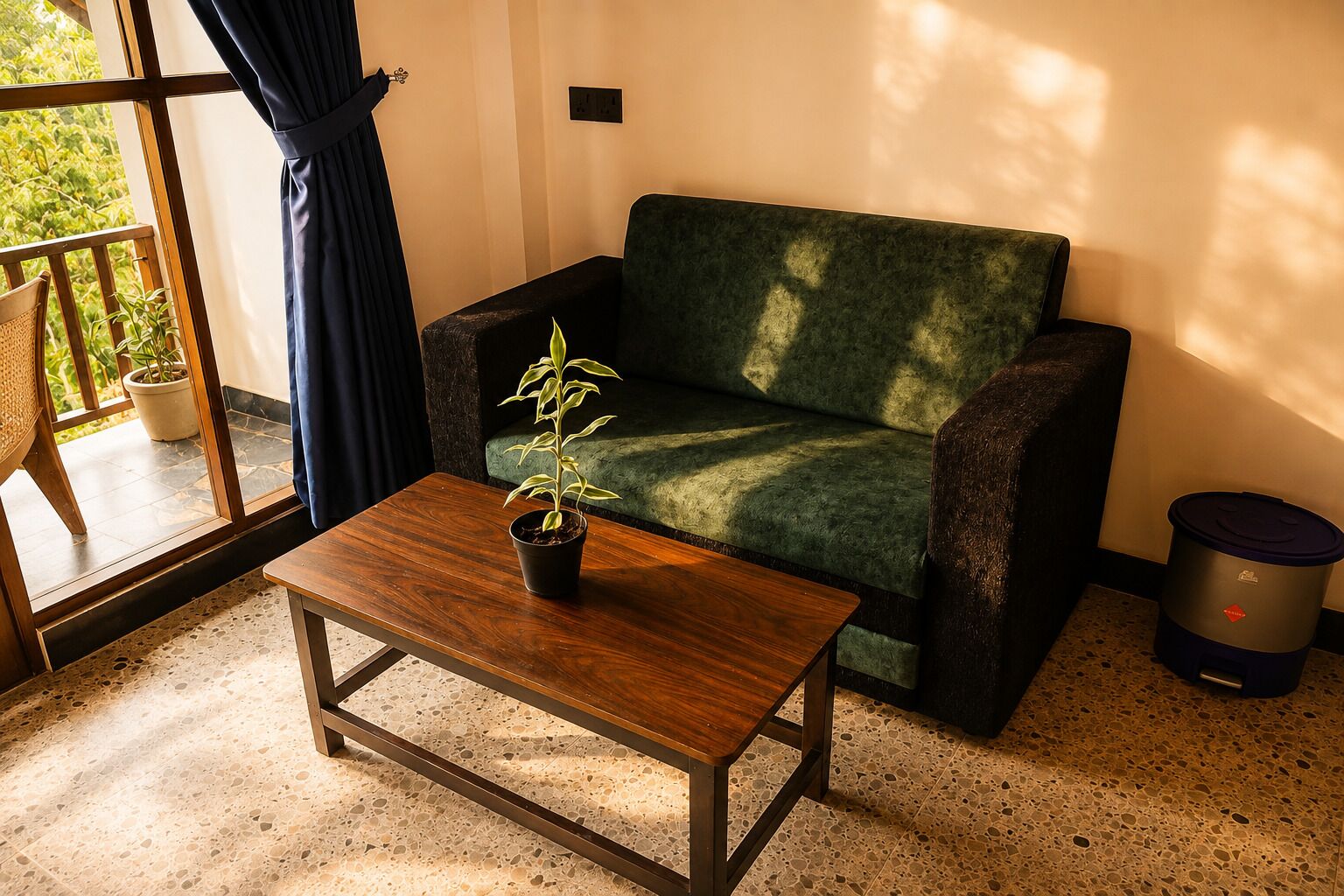 Une pièce avec un canapé vert, une table basse en bois, une plante en pot, une poubelle et une vue par la fenêtre.