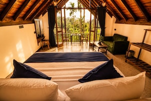 A bedroom with a large bed, a view of greenery, and a wooden ceiling.