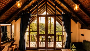 A room with a sloped wooden ceiling, large windows, and a view of a lush landscape.