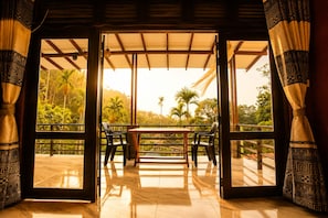 Una habitación amplia con una mesa y sillas, ventanas grandes con cortinas, y vistas a zonas verdes al exterior.