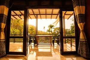 Una habitación amplia con una mesa y sillas, ventanas grandes con cortinas, y vistas a zonas verdes al exterior.