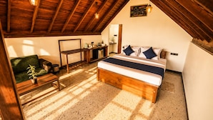 A bedroom with a wooden bed, a green sofa, a small table, and a kitchen area.