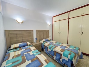 A bedroom with two beds, a wardrobe, and bedside lamps. - Edificio Playa (Los Cristianos)