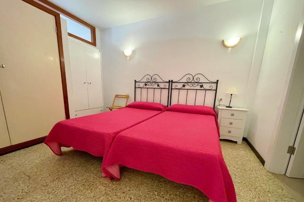 Una habitación con cama doble, armario, mesita de noche y dos luces en la pared.
