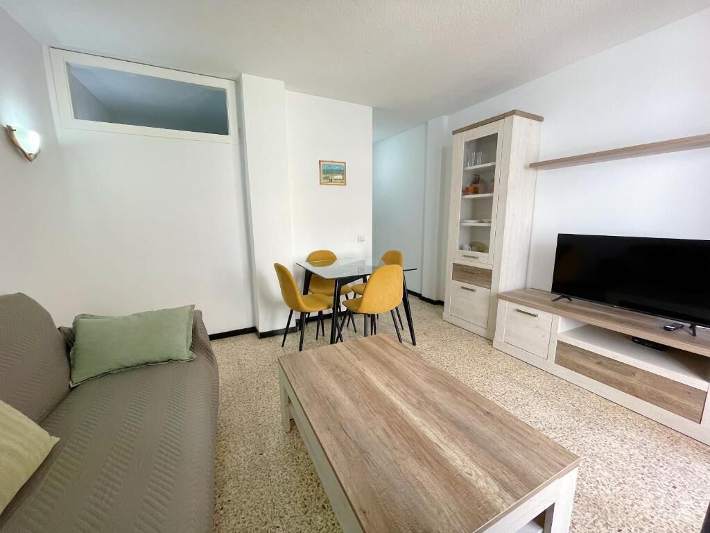 Una sala de estar con sofá, mesa de centro, televisor, mesa de comedor con sillas y un mueble aparador.