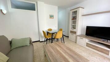 Una sala de estar con sofá, mesa de centro, televisor, mesa de comedor con sillas y un mueble aparador.