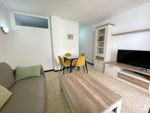 Una sala de estar con sofá, mesa de centro, televisor, mesa de comedor con sillas y un mueble aparador.