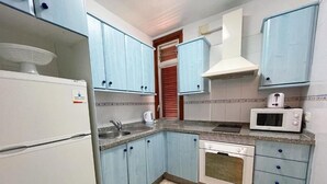 A kitchen with light blue cabinets, a white refrigerator, a microwave, and a stove. - Edificio Playa (Los Cristianos)