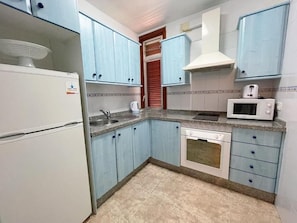 A kitchen with light blue cabinets, a white refrigerator, a microwave, and a stove. - Edificio Playa (Los Cristianos)