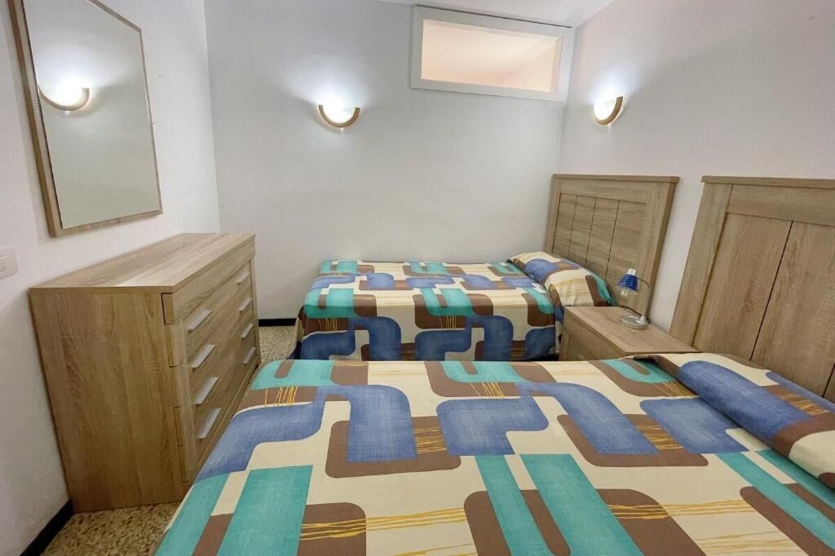 Un dormitorio con dos camas, un aparador de madera y luces fijadas a la pared.