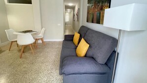 A modern living room with a grey sofa, two yellow cushions, a white coffee table, and a white floor lamp. - Edificio Playa (Los Cristianos)