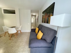 A modern living room with a grey sofa, two yellow cushions, a white coffee table, and a white floor lamp. - Edificio Playa (Los Cristianos)