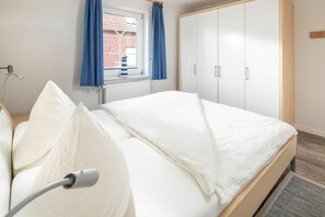 Ein Schlafzimmer mit Bett, einem Fenster mit Vorhängen, einem Heizkörper und einem Kleiderschrank.