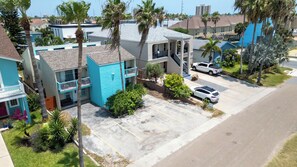 A residential area with a two-story house featuring a balcony, a parked white SUV, and a clear sky. - 2BR Ground Floor, Sleeps 8, Pets ok - SPI (South Padre Island)