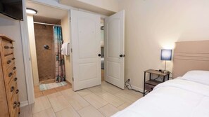 A hotel room with a bed, a bedside table with a lamp, a shower area, and a wooden wardrobe. - 2BR Ground Floor, Sleeps 8, Pets ok - SPI (South Padre Island)