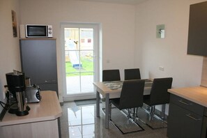 Eine kompakte Küche mit einer Mikrowelle, einem Toaster und einer Kaffeemaschine auf der Arbeitsfläche, einem Esstisch mit Stühlen und einer Glastür zu einem Außenbereich.