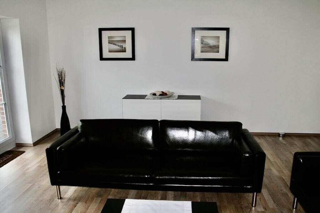 A modern living room with a black leather sofa, a white cabinet, and two framed pictures on the wall.
