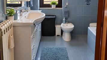 Une salle de bain moderne avec un grand lavabo, des toilettes et un bidet. Une fenêtre laisse entrer la lumière naturelle et offre une vue sur la verdure environnante.