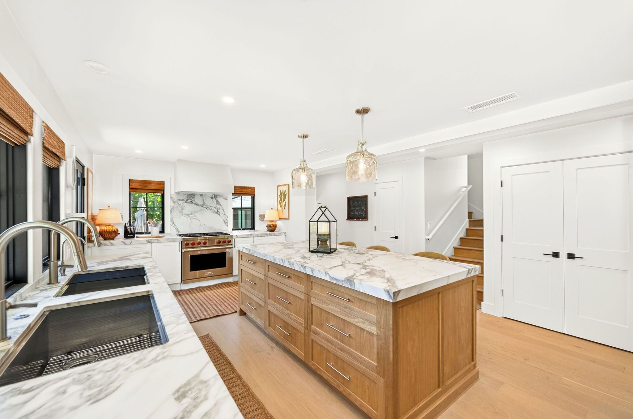 A modern kitchen with a marble countertop, wooden cabinets, stainless steel appliances, and pendant lighting.