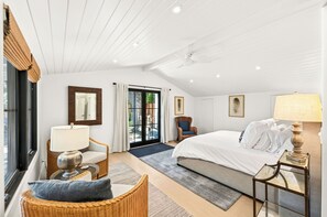Ein Schlafzimmer mit einem Bett, einem Sessel, einem Tisch, einer Lampe und einem Fenster.