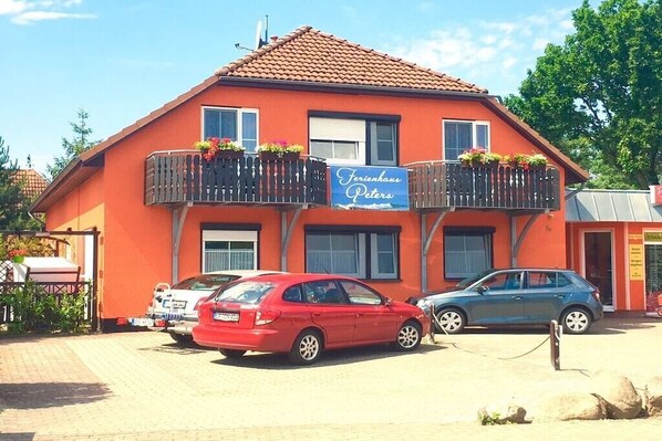 A two-story building with a red facade, a sign reading 'Ferienhaus Peters,' and two cars parked in front. - Holiday apartment with 1 bedroom (Prerow)