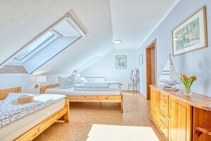 Ein Schlafzimmer mit schrägem Dach, Oberlichtern, einem Bett, einer Kommode und einem kleinen Tisch mit einer Lampe.