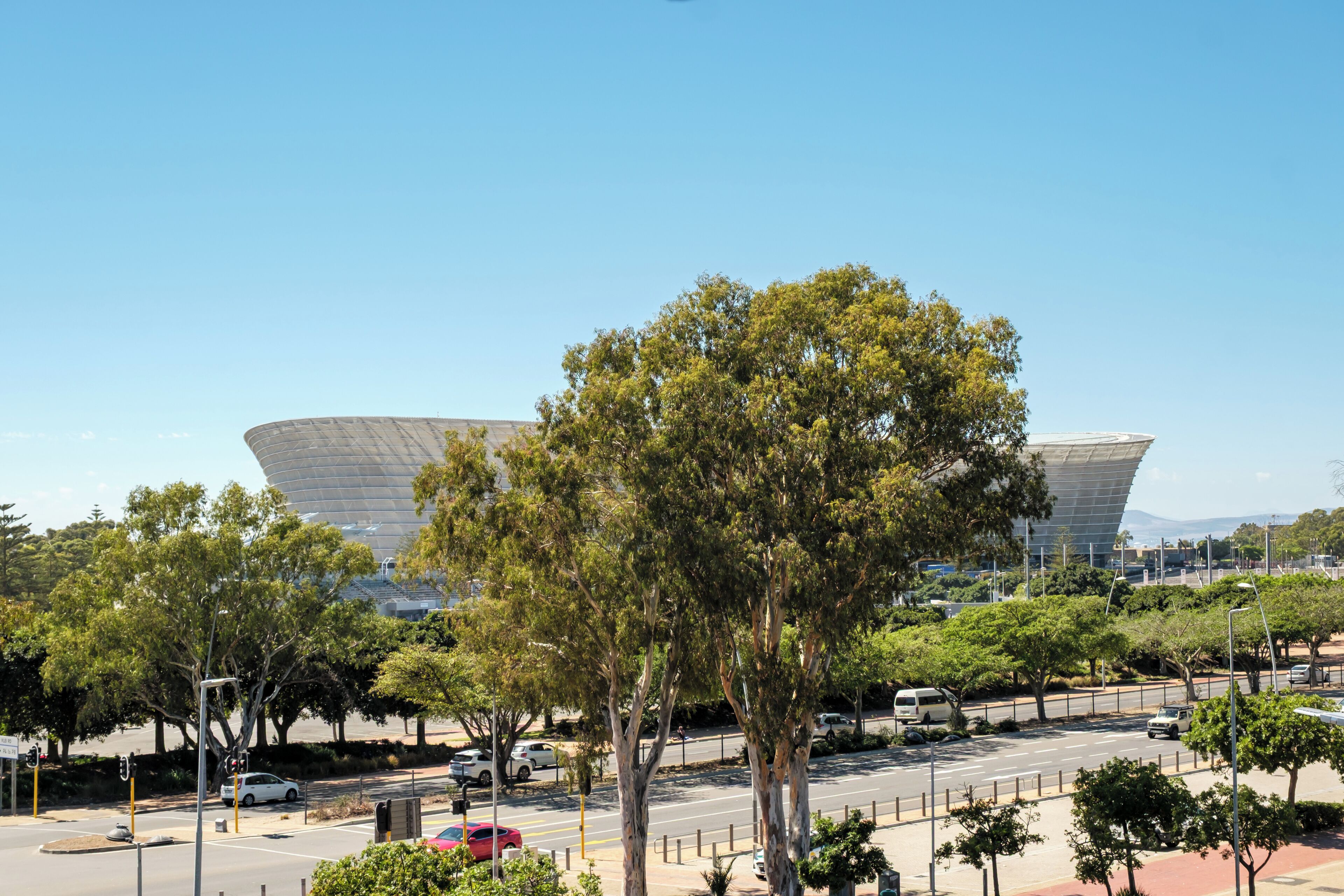 A modern building with a unique curved roof, surrounded by lush green trees and a clear blue sky.