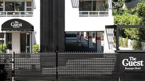 Un edificio de varios pisos con un llamativo letrero vertical que dice 'The Guest Boutique Hotel'.
